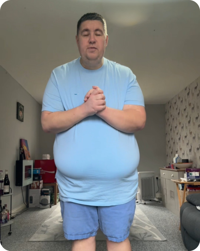 Man with blue shorts and t-shirt stood up inside a living room