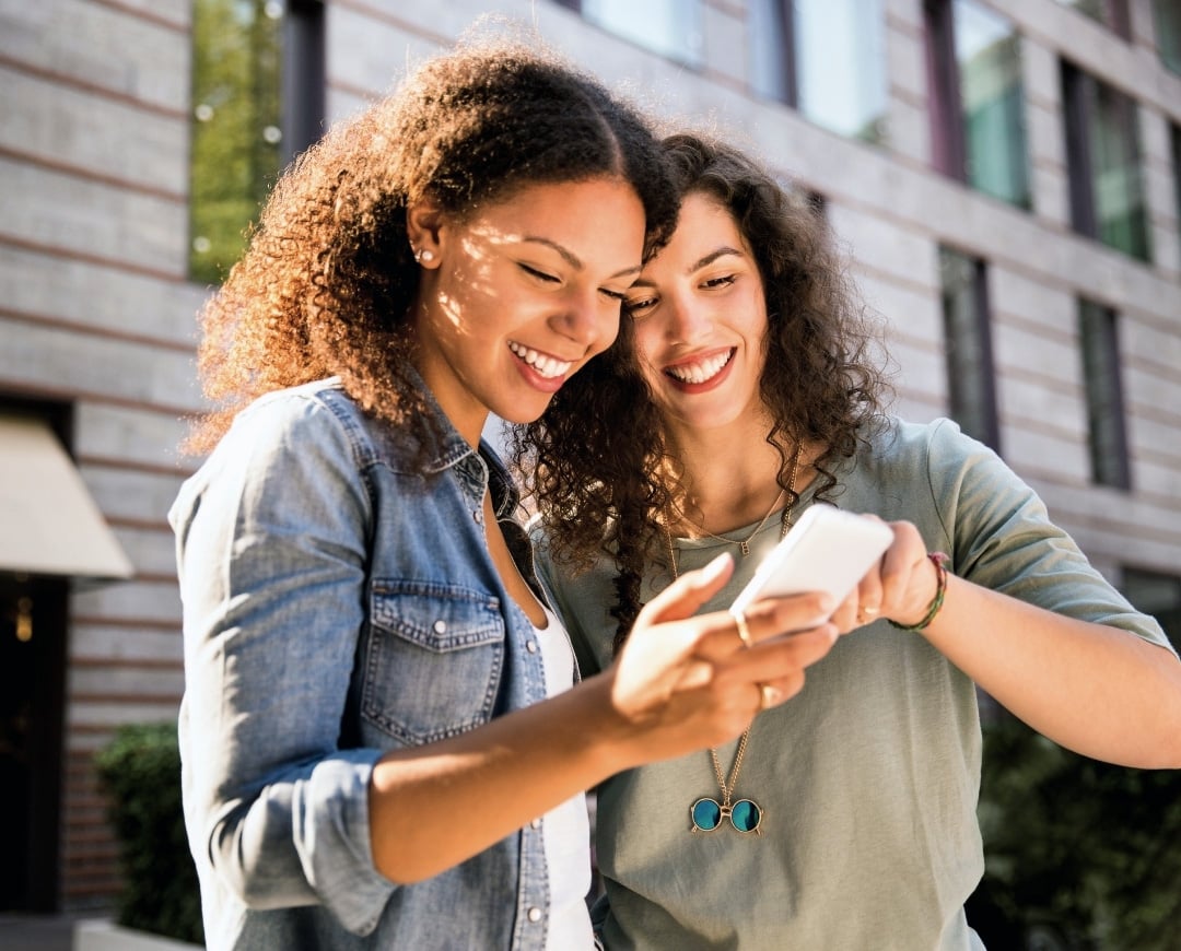 refer a friend two women looking at a phone and smiling