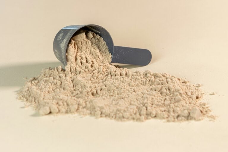 Protein powder spilled from a measuring scoop onto a light beige surface.